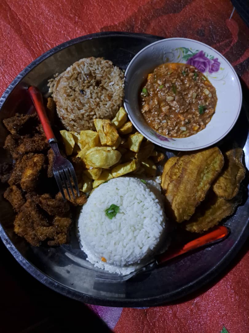 A plate of fried fish, fried matooke, white rice and stew