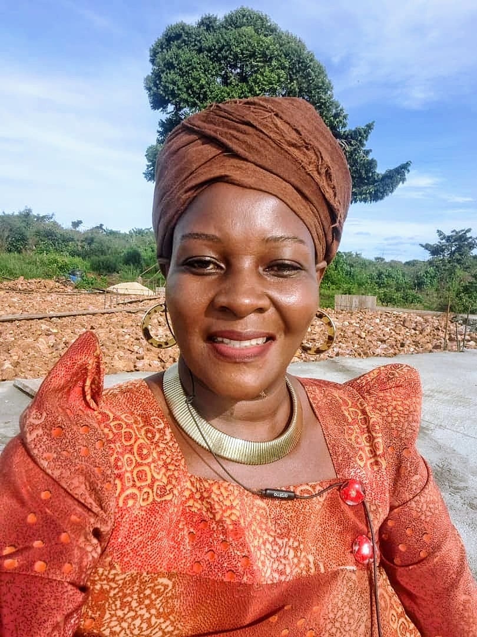 Queen Nalubaale outdoors in a brown headwrap and gold collar